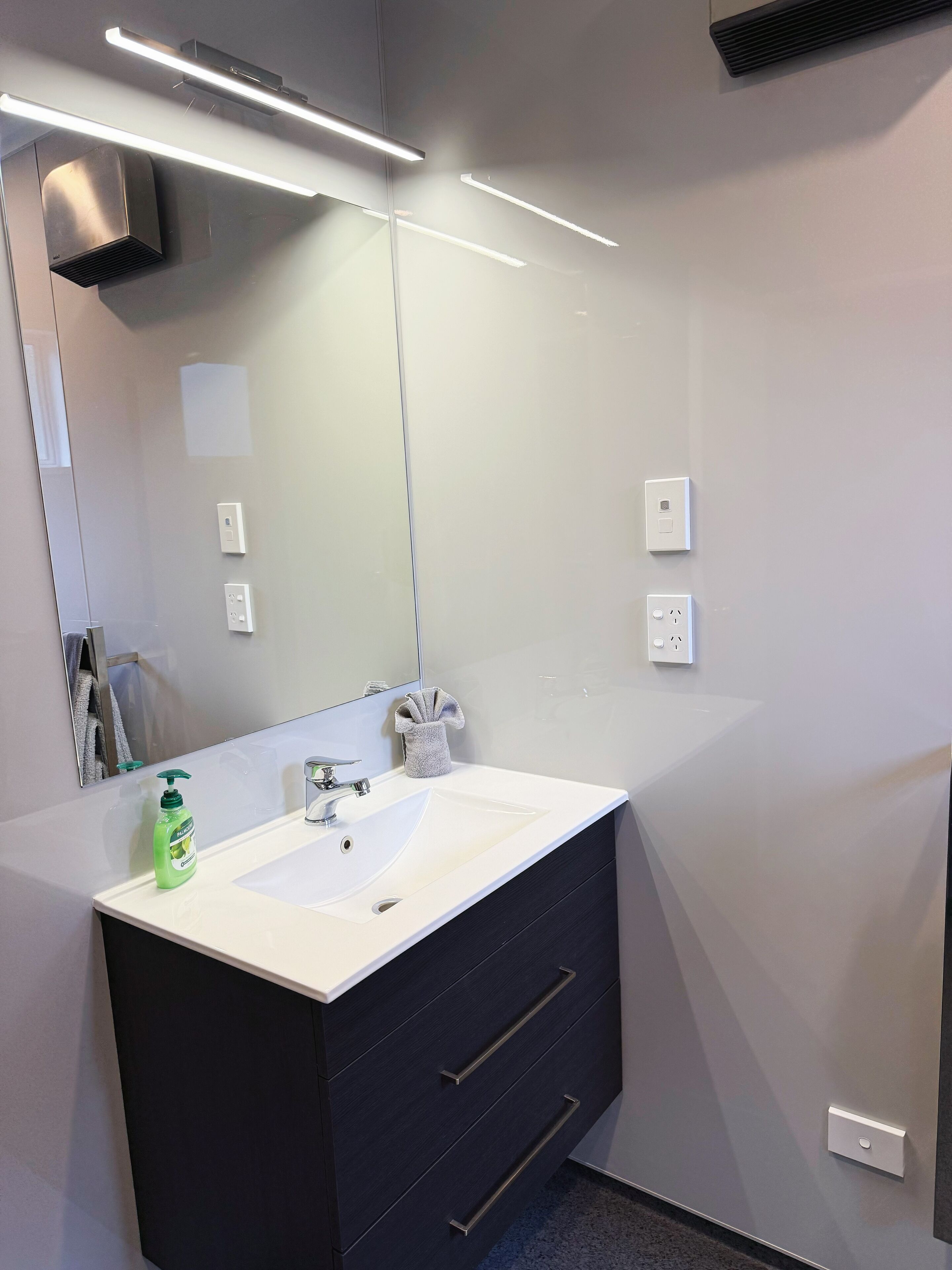 Un baño moderno con un lavamanos blanco, muebles oscuros y un espejo grande.