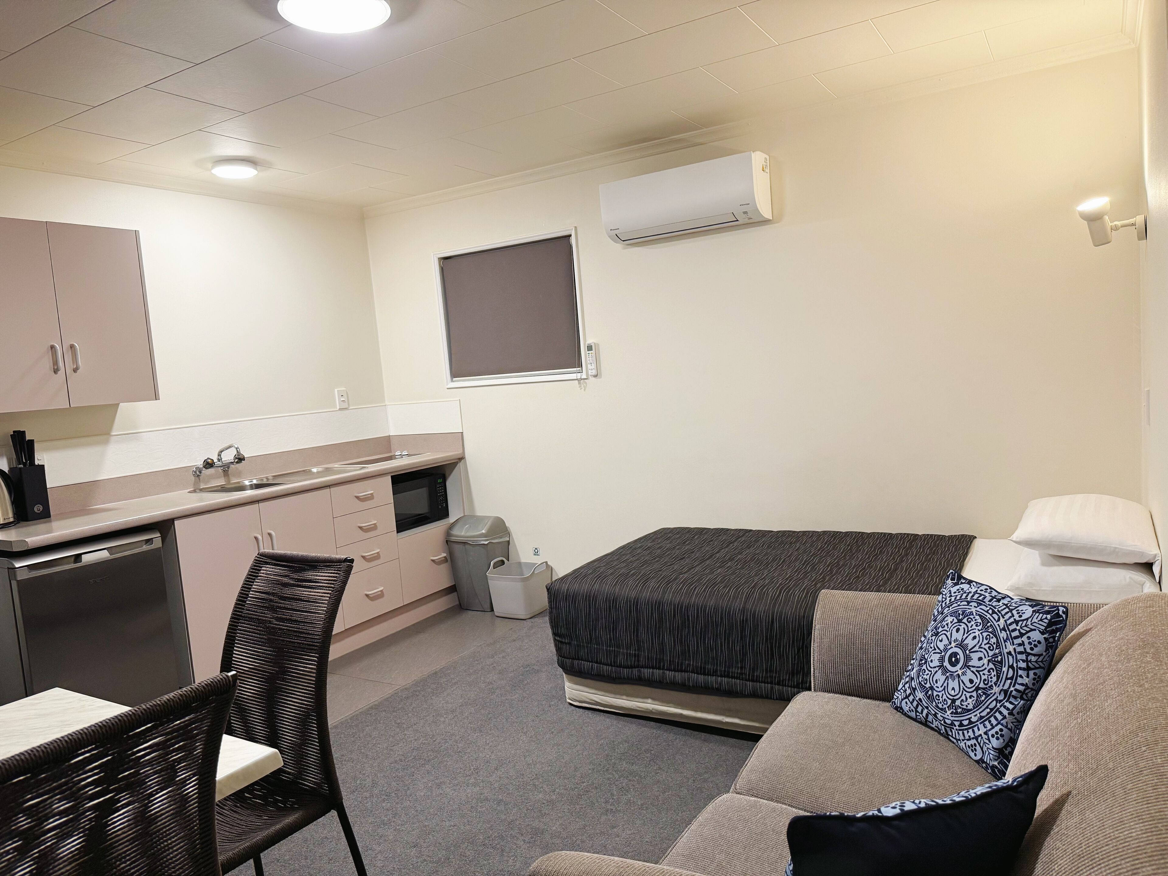 A compact room with a kitchenette, a bed, a seating area, and a window.
