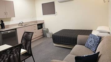 A compact room with a kitchenette, a bed, a seating area, and a window.