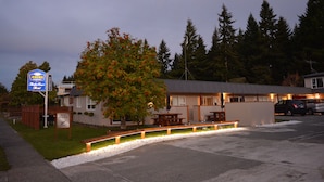 A motel with a signboard, a tree with red flowers, and a parking area. - Amber Court Motel (Te Anau)