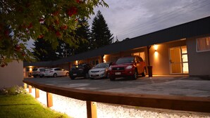 A parking area with several cars parked in front of a building with a sloped roof and a wooden deck. - Amber Court Motel (Te Anau)