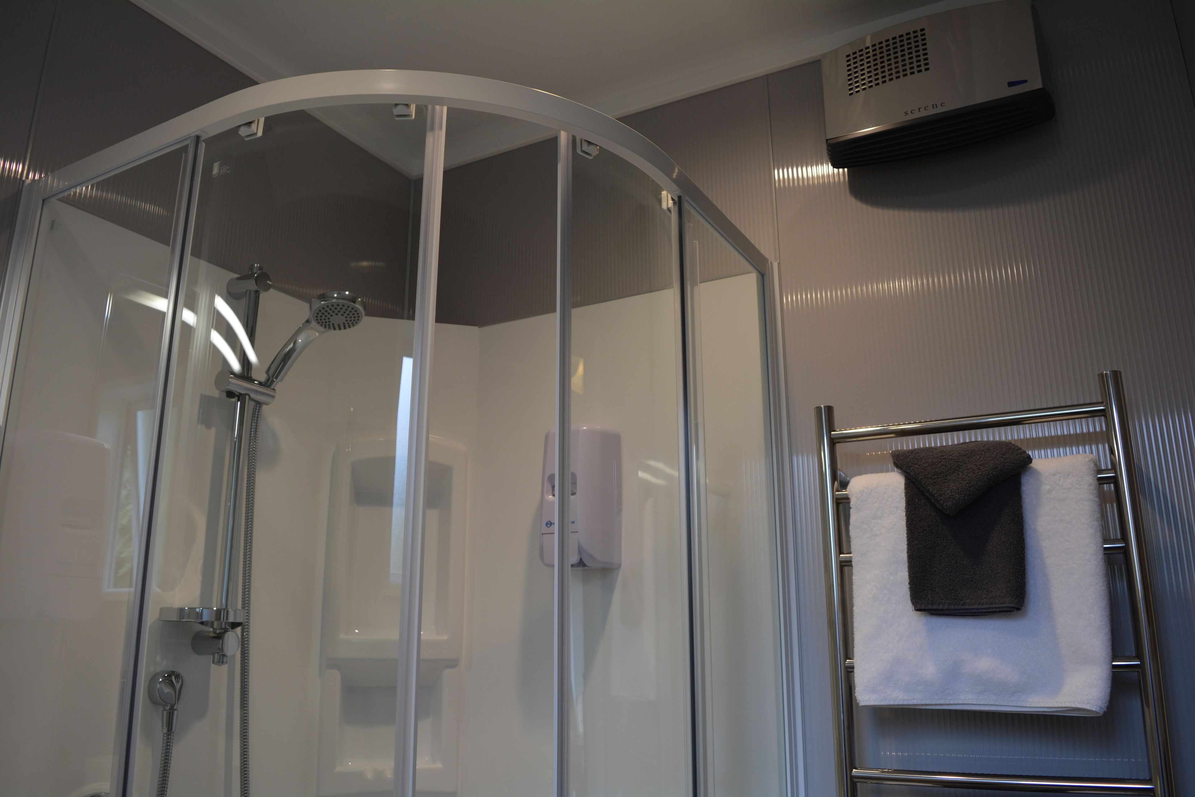 A glass-enclosed shower with a handheld showerhead, a towel rack with a folded towel, and a wall-mounted air conditioner.