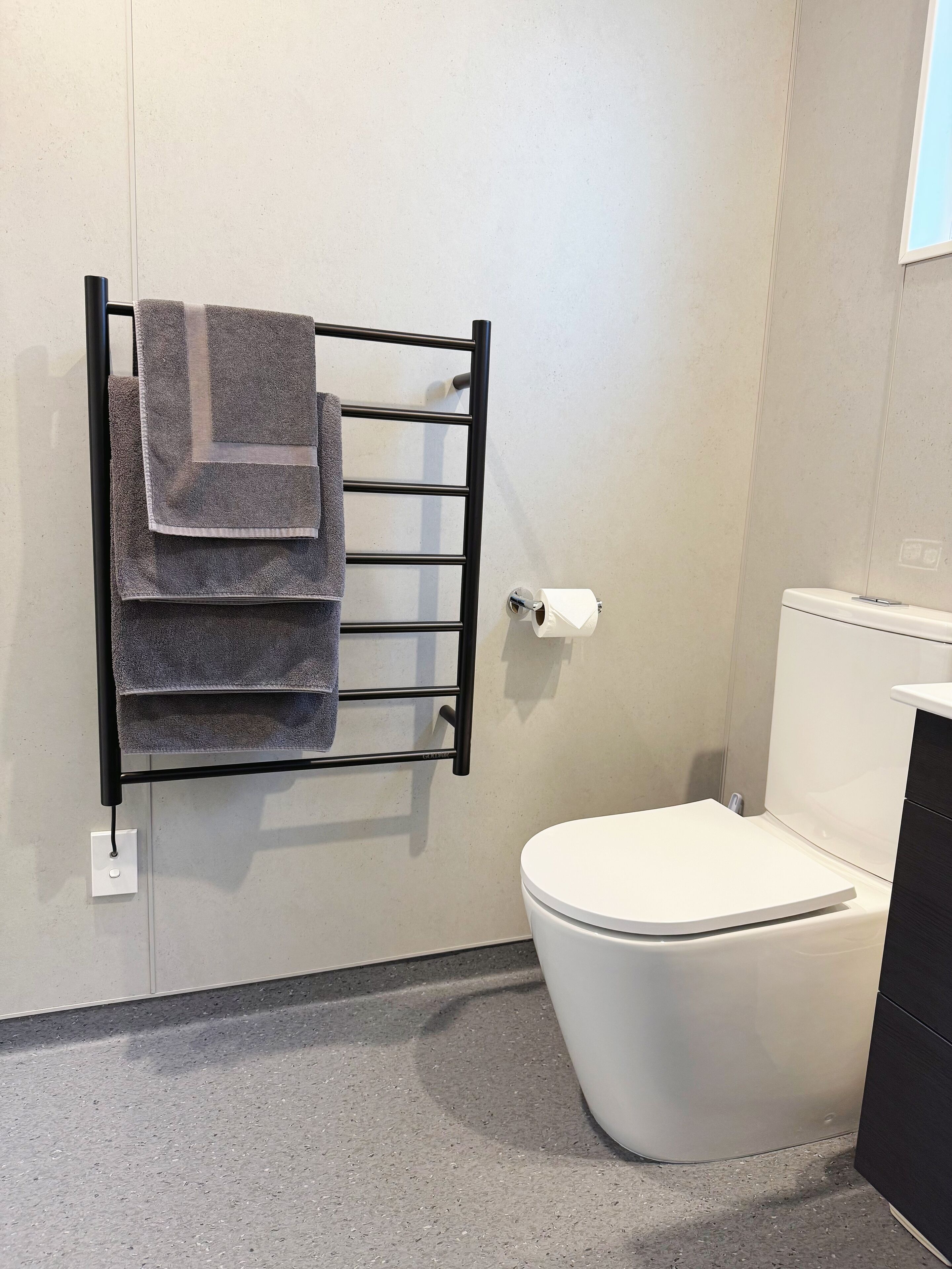 Une salle de bain avec des toilettes blanches, un porte-serviettes avec des serviettes pliées et un support à papier toilette.