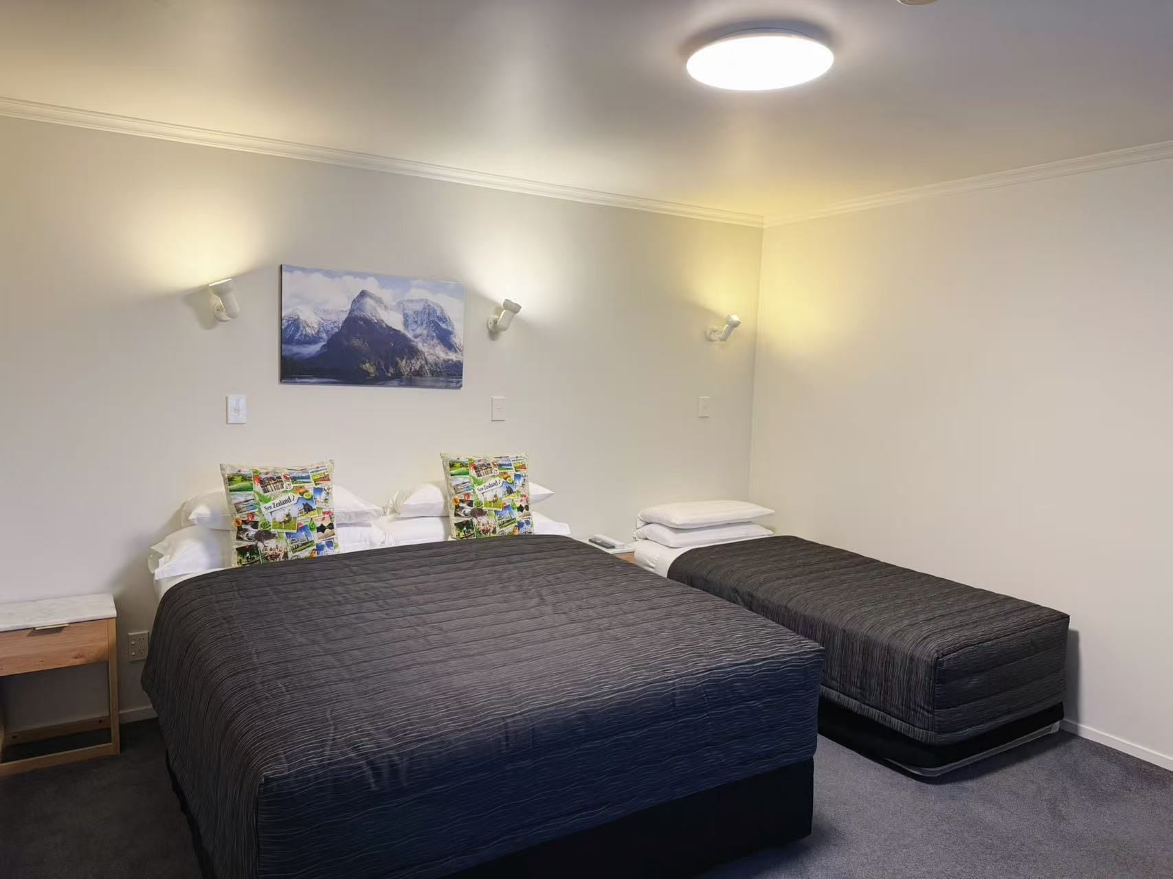 A hotel room with two beds, a nightstand, a desk, and a wall-mounted picture.