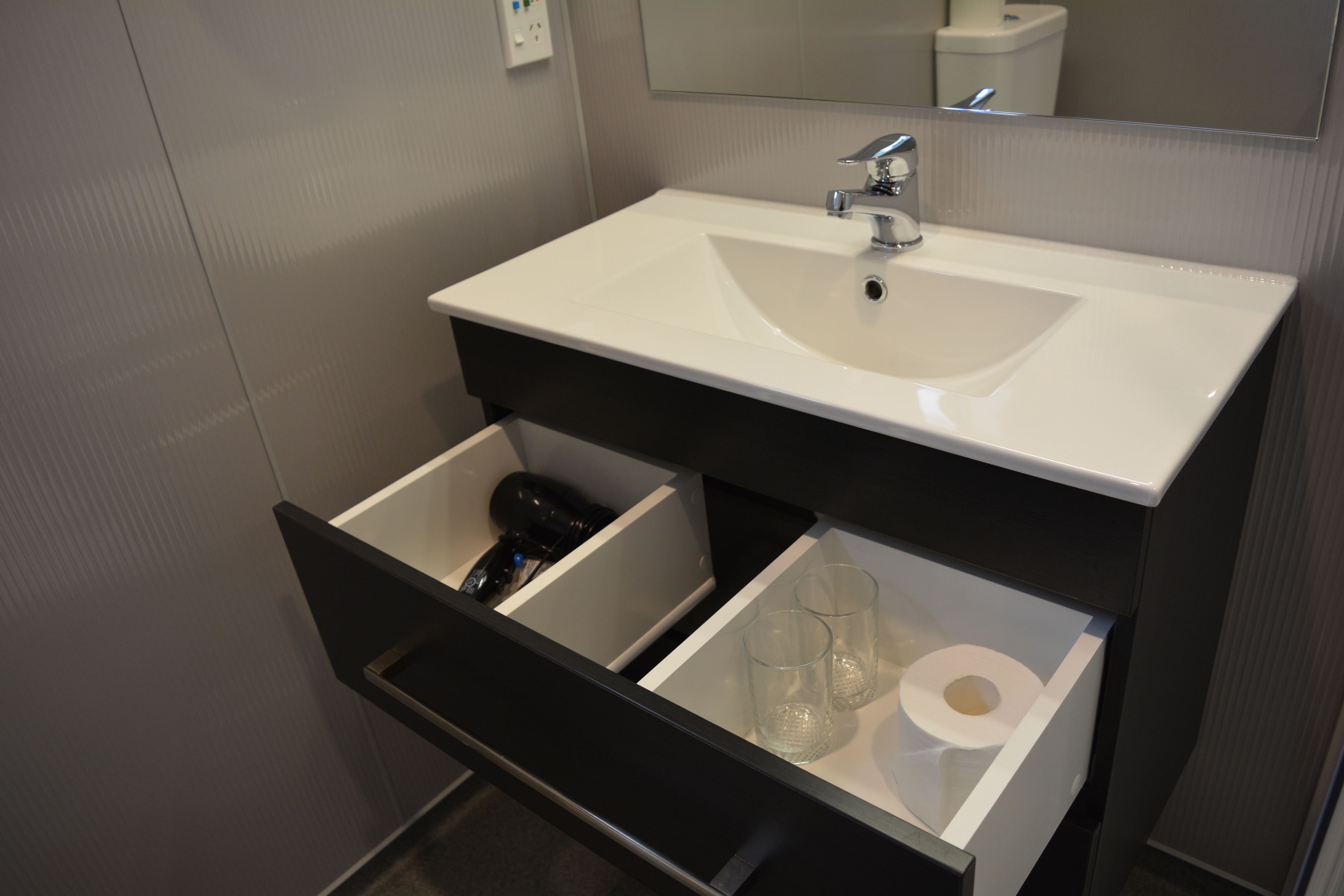 A bathroom with a white sink, a mirror above it, and a black drawer below.
