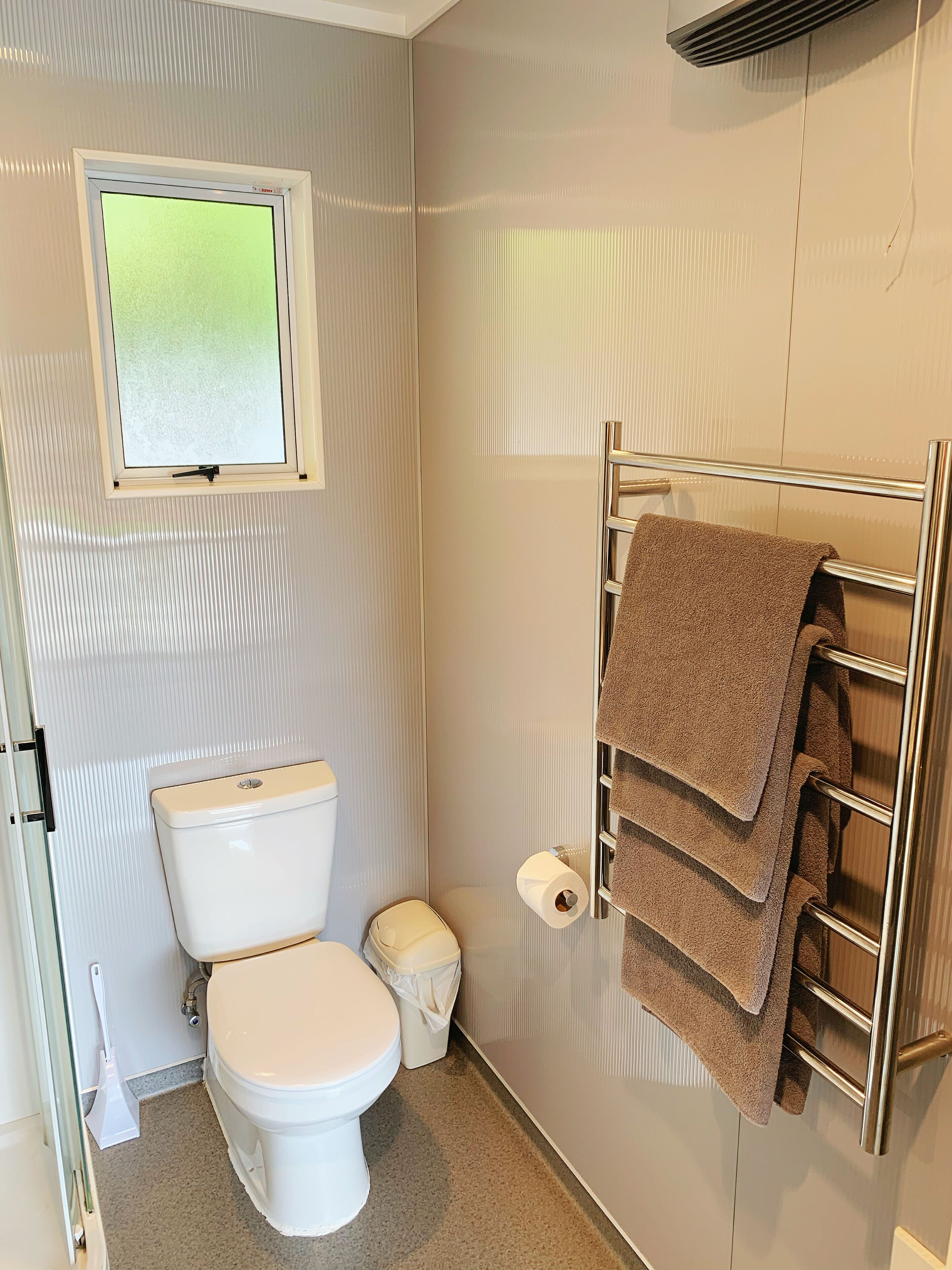 A bathroom with a toilet, a towel rack with towels, a window, and a toilet paper holder.