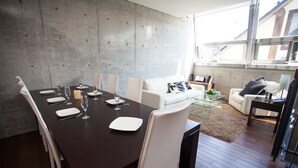 A modern dining area with a dark wooden table set for six, white chairs, and a white sofa in the background. - Full Circle (Kutchan)