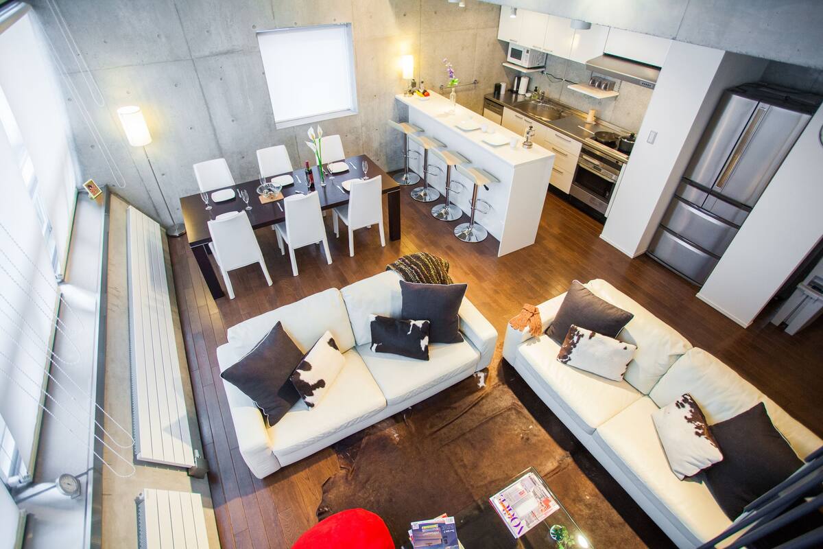 A modern kitchen with a central island, white bar stools, and a dining area with a table and chairs.
