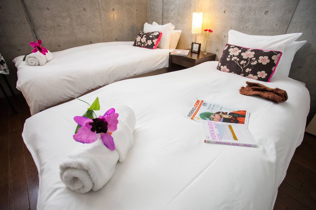 A hotel room with two beds, each with white linens, pillows, and a small bedside table with a lamp and a magazine.