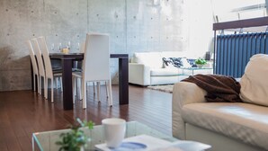 A modern living room with a dining area, featuring a glass coffee table, white chairs, a sofa, and a blue-framed window. - Full Circle (Kutchan)