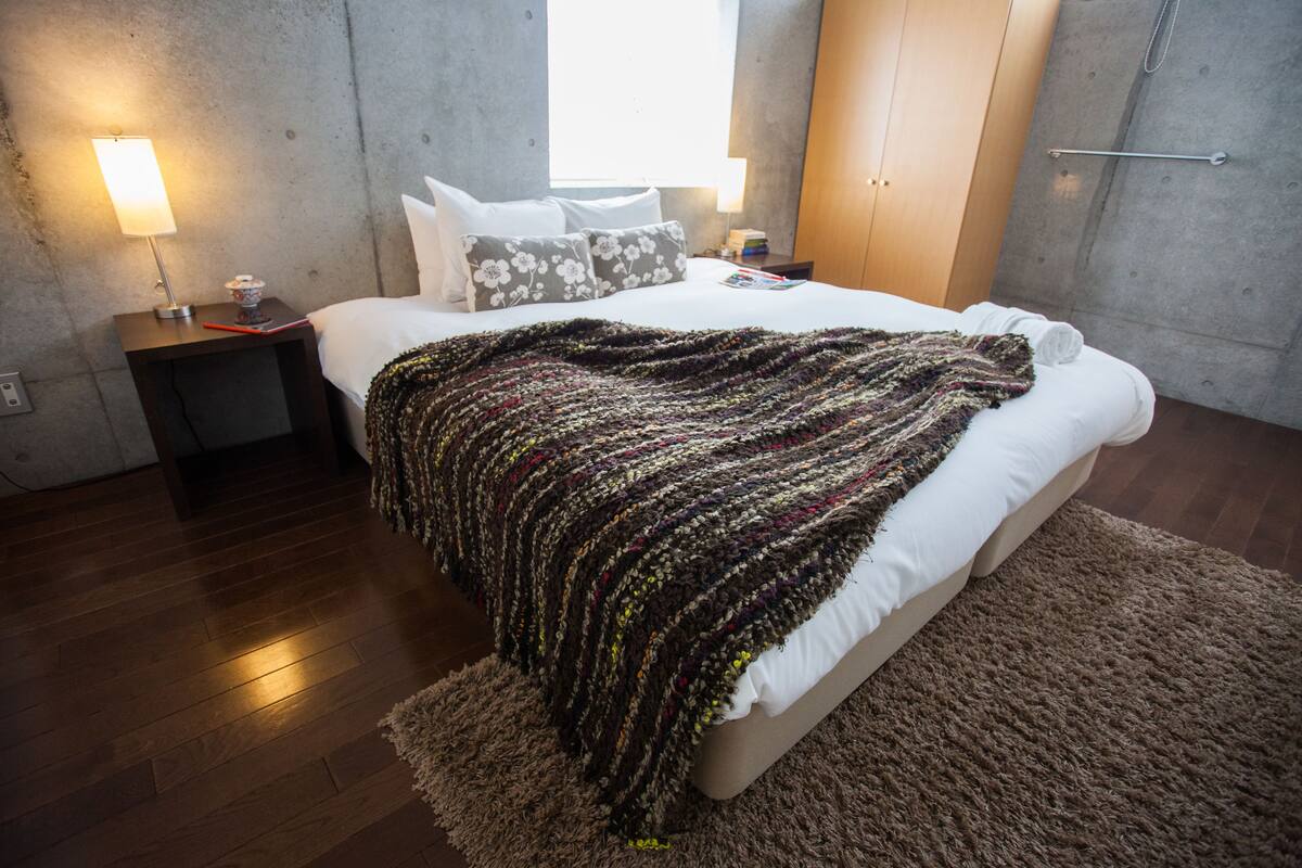 A modern bedroom with a large bed, a wooden floor, and a concrete wall.