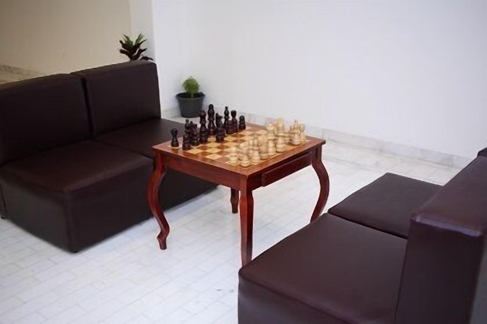 A living room with a wooden chess table, dark brown sofas, and a potted plant.