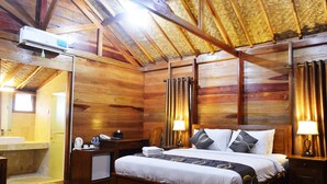Een houten kamer met een bed, nachtkastje, lamp en een badkamer met wastafel en spiegel.