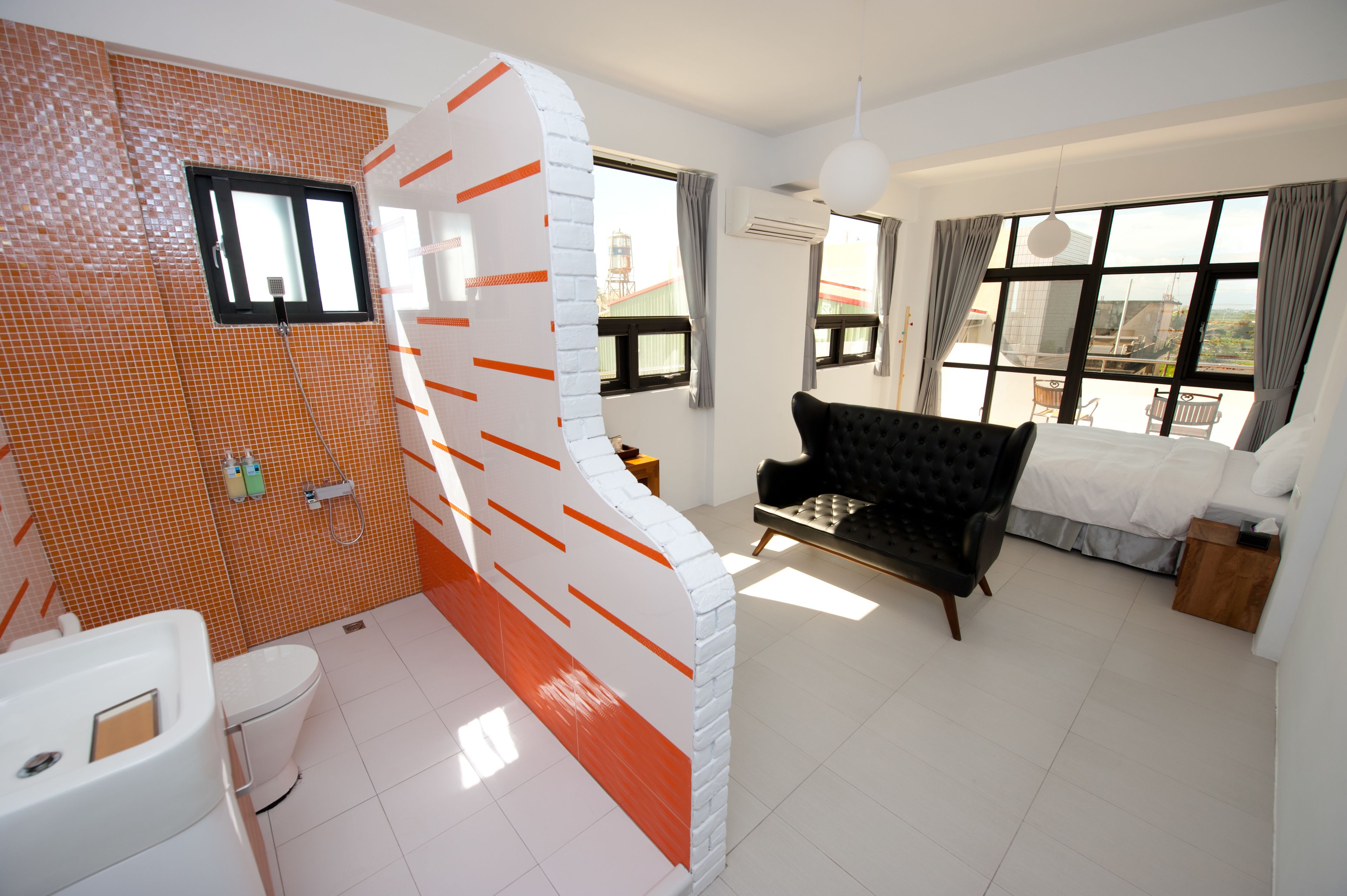 A modern hotel room with a bathroom, a sofa, a bed, and a view of the city.