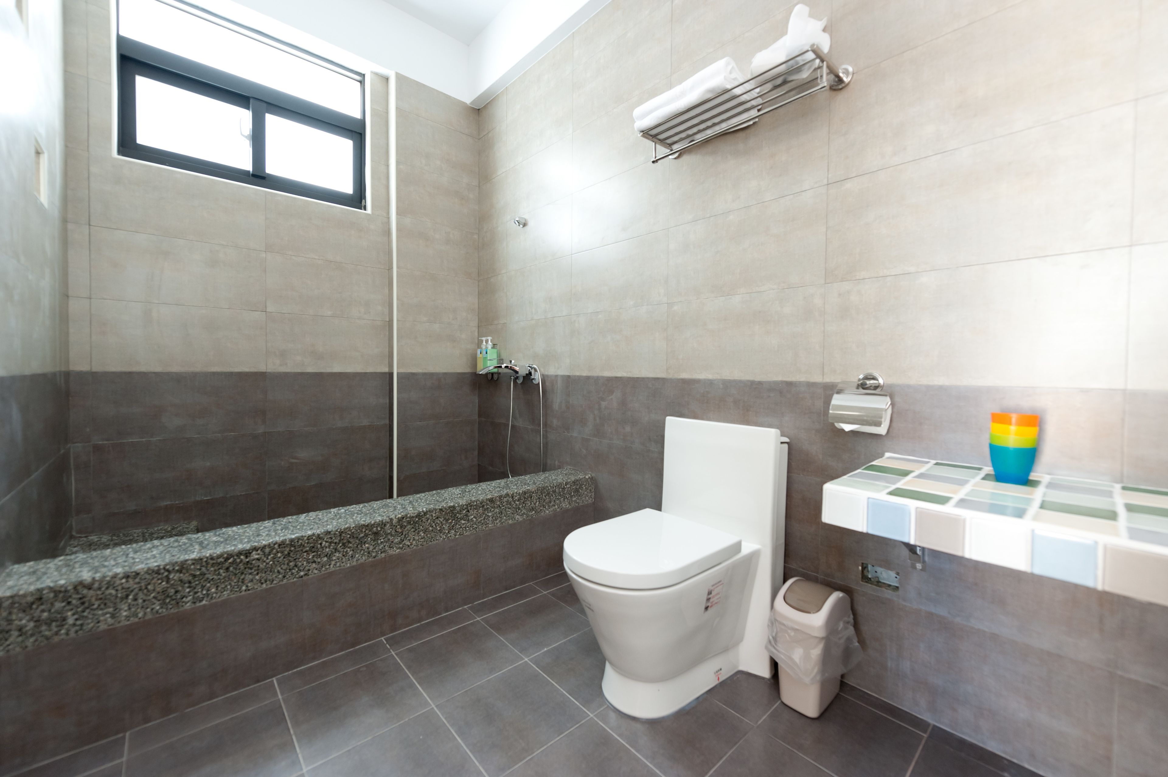 A modern bathroom with a shower, toilet, and a small shelf with toiletries.