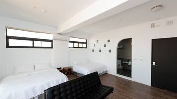 Habitación de hotel moderna con dos camas, un sofá negro y un baño visible a través de un arco.