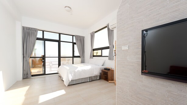 Un dormitorio moderno con una cama grande, televisión y puerta corrediza de cristal que da a un balcón.