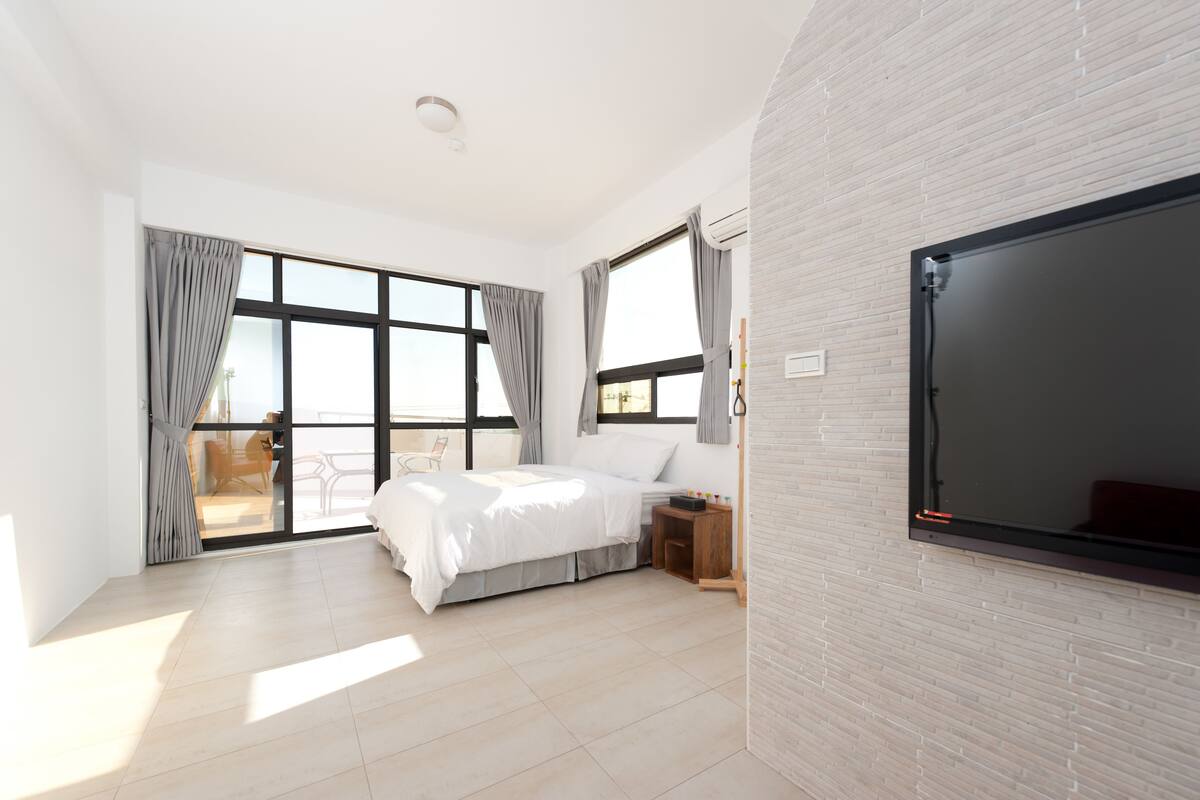A modern bedroom with a large bed, a TV, and a sliding glass door leading to a balcony.