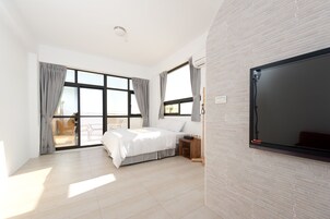 Un dormitorio moderno con una cama grande, televisión y puerta corrediza de cristal que da a un balcón.