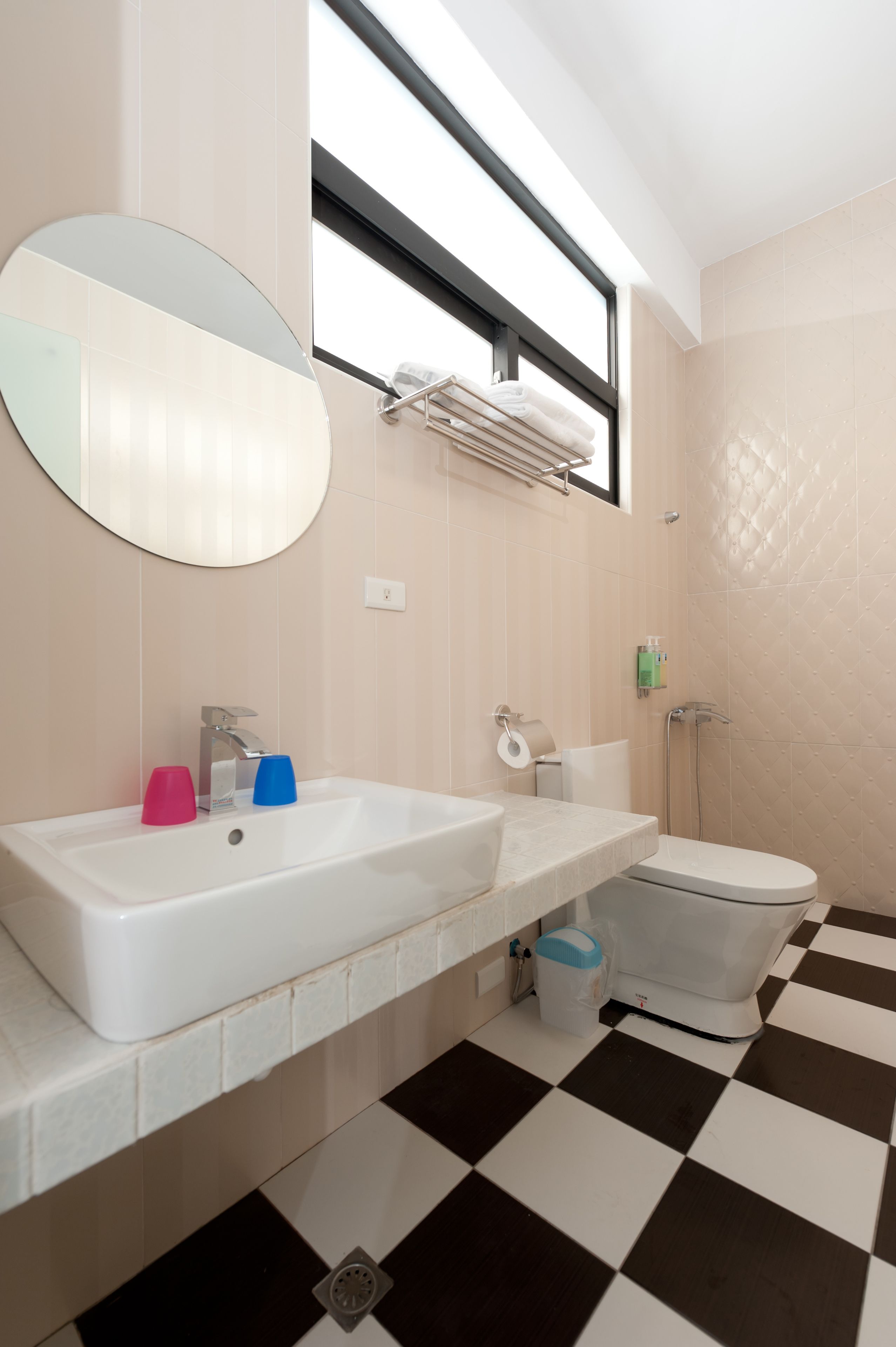 A bathroom with a white sink, a mirror, and a toilet. There is a window above the sink and a shower area to the right.