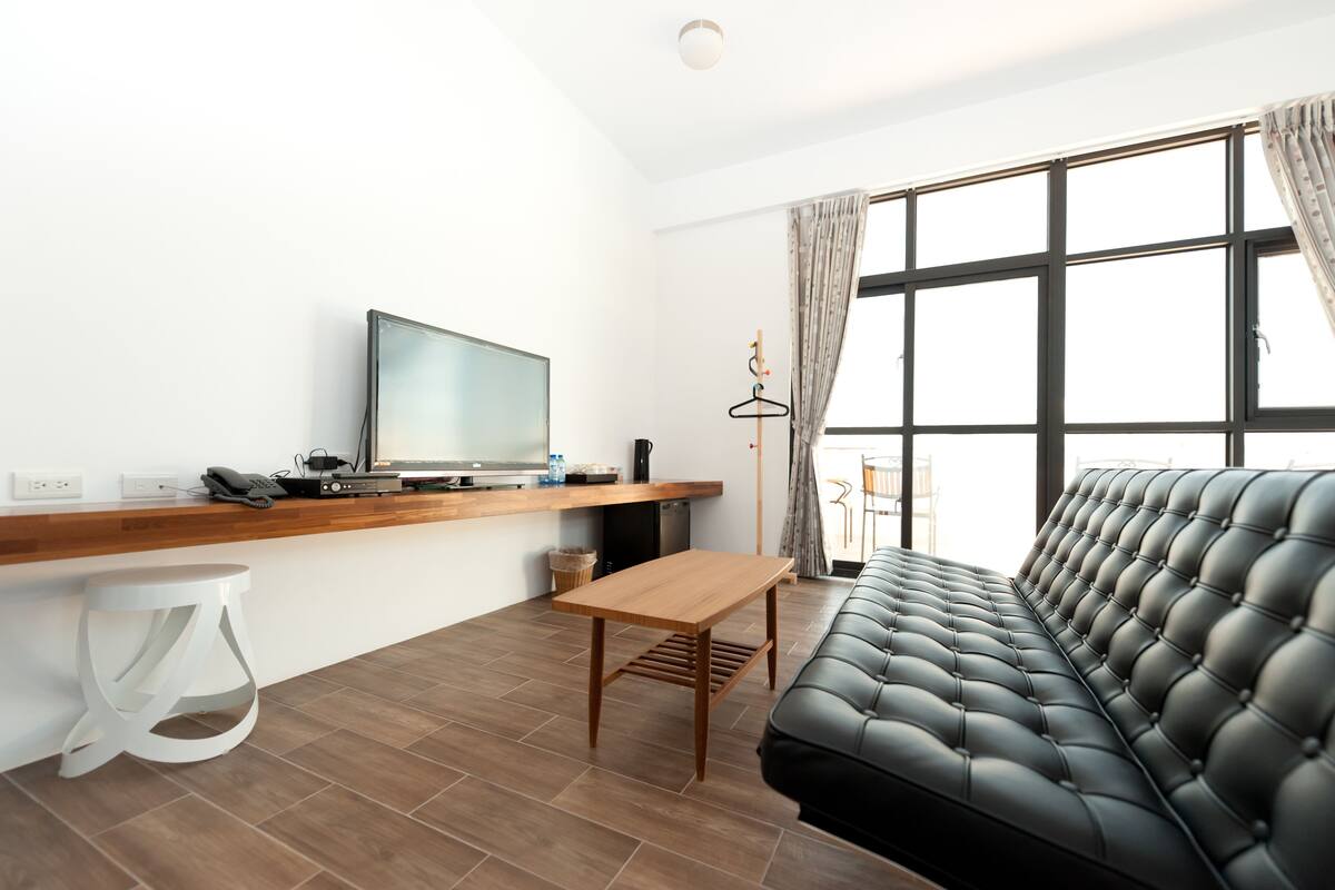 A modern living room with a sofa, a wooden table, a TV, and a hanging light fixture.