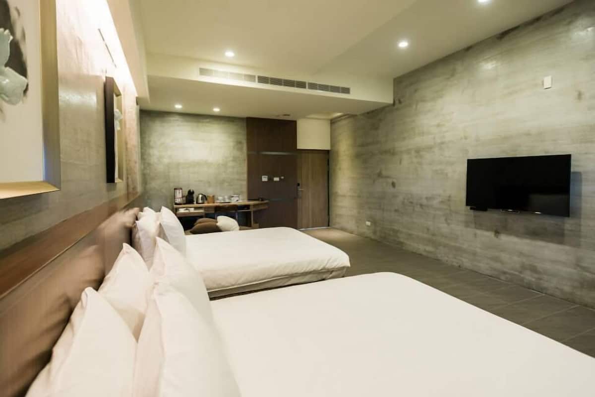Habitación de hotel con dos camas, un escritorio, un televisor de pantalla plana en la pared y un ventanal grande.