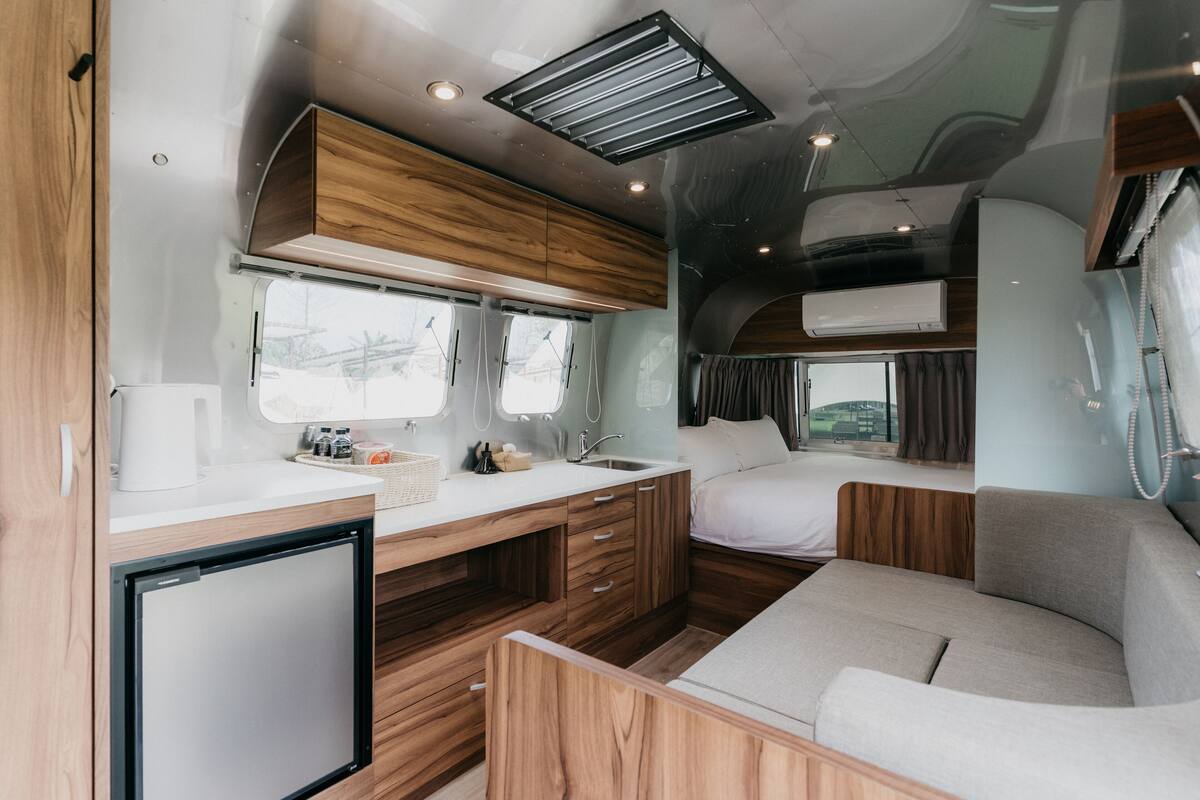 Interior compacto de autocaravana con kitchenette, cama y zona de estar.