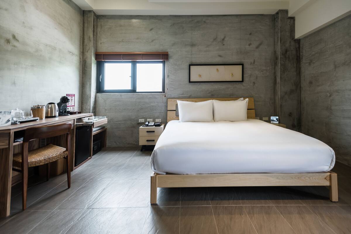 Un dormitorio con una cama de madera, un escritorio con silla, una mesita de noche y una ventana con persianas.