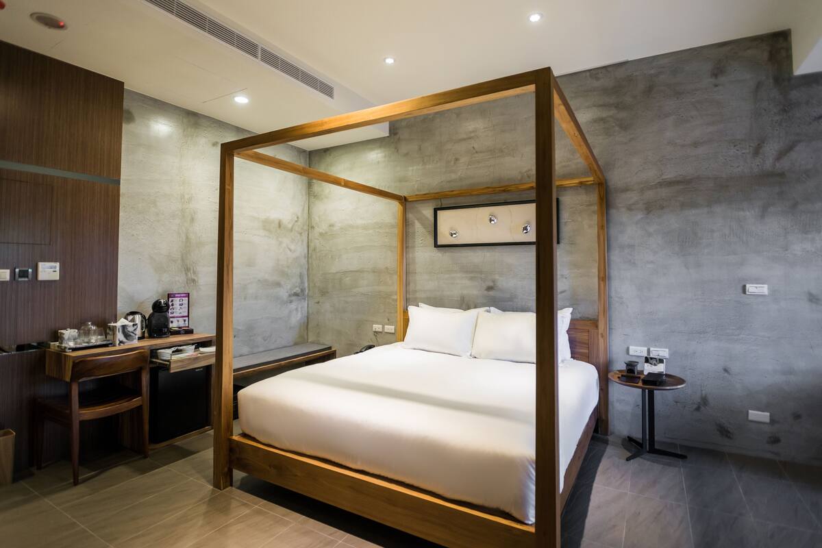Habitación de hotel moderna con cama con dosel, un escritorio de madera con silla, una mesita y una cafetera.