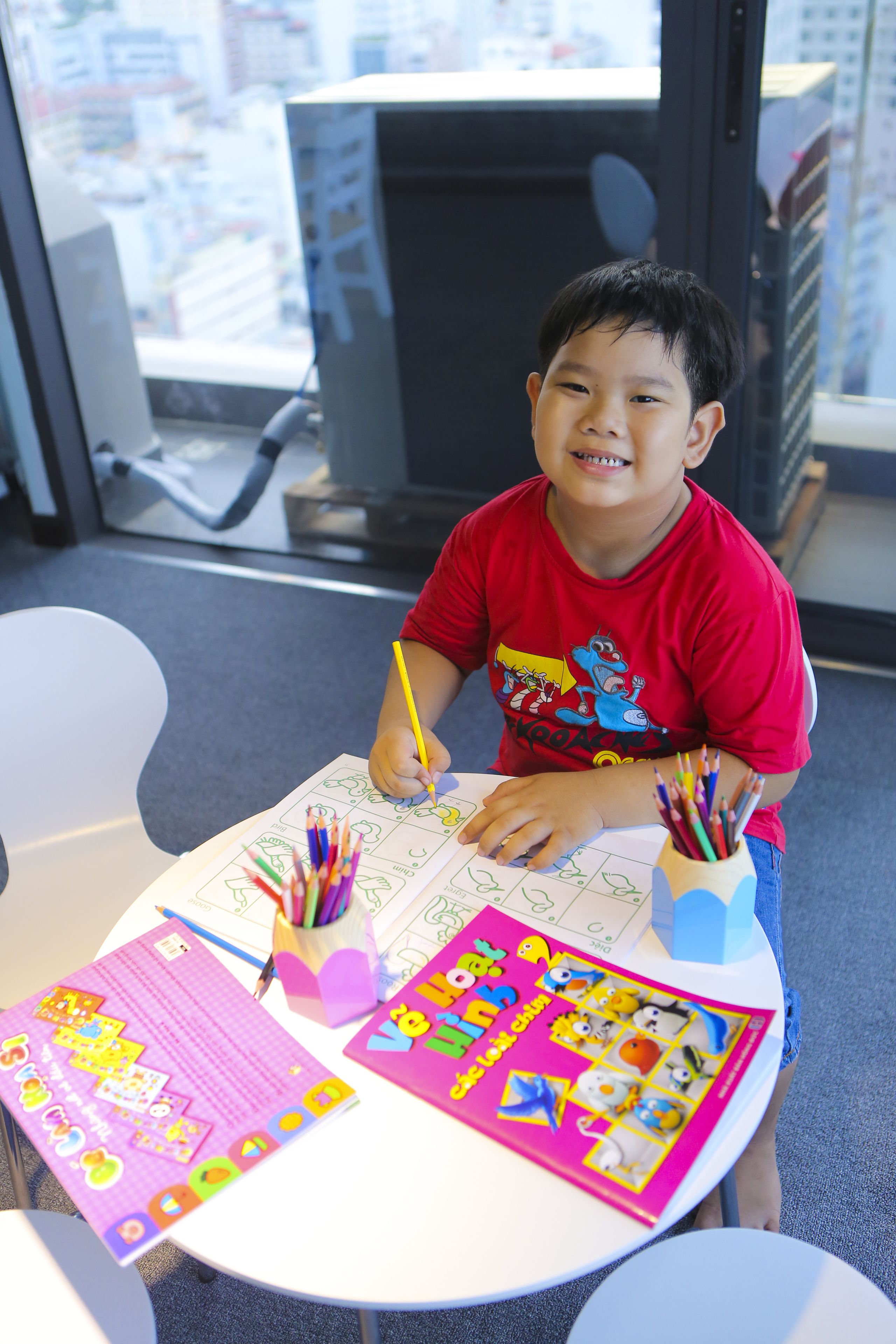 A child drawing at a table with art supplies and coloring books.