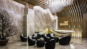 Een moderne lobby met een marmeren wand, een receptiebalie en zwarte rieten stoelen.
