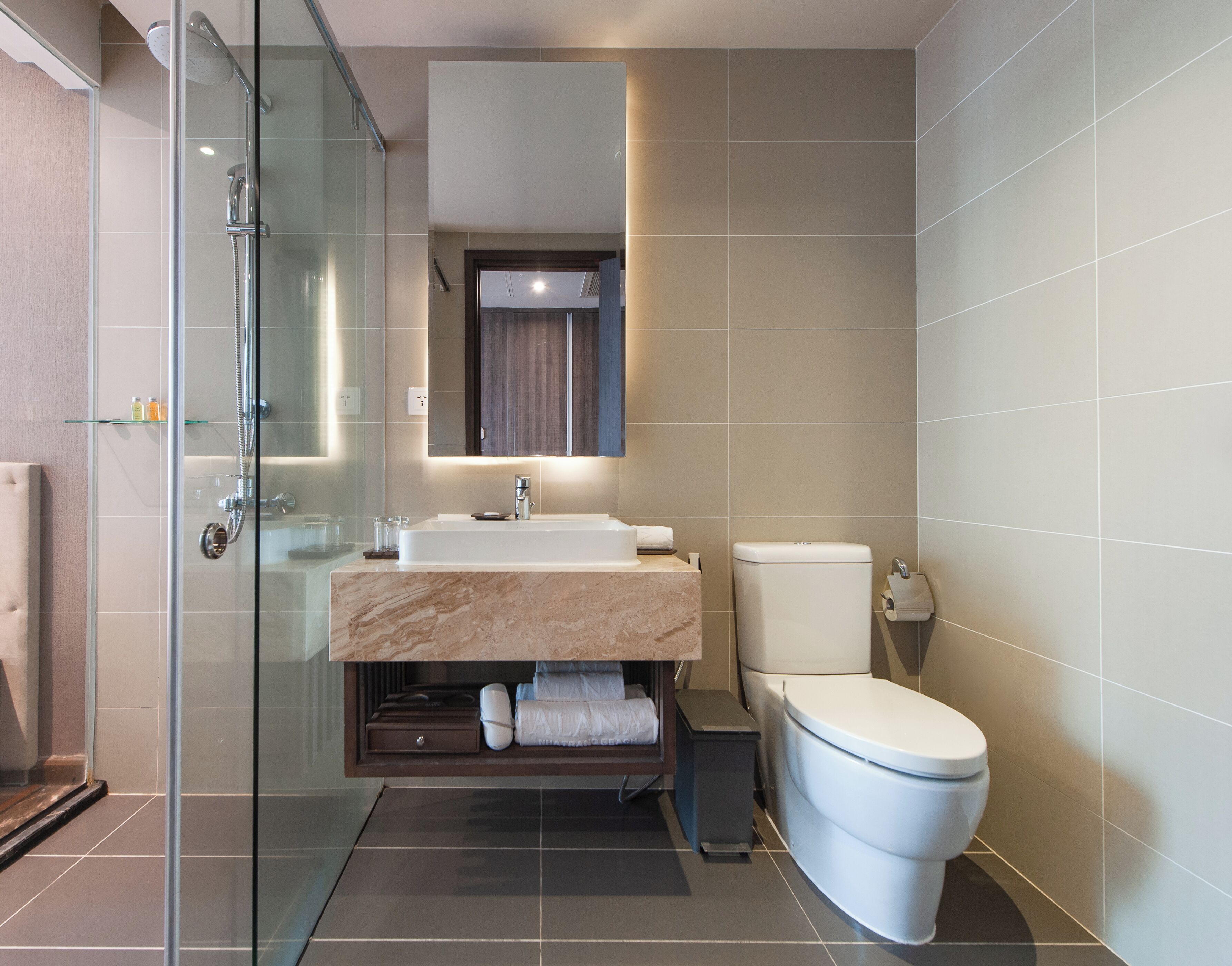 A modern bathroom with a glass-enclosed shower, a marble sink, a toilet, and a small mirror above the sink.