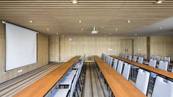 A conference room with long tables and chairs, a projector screen, and a wooden ceiling.