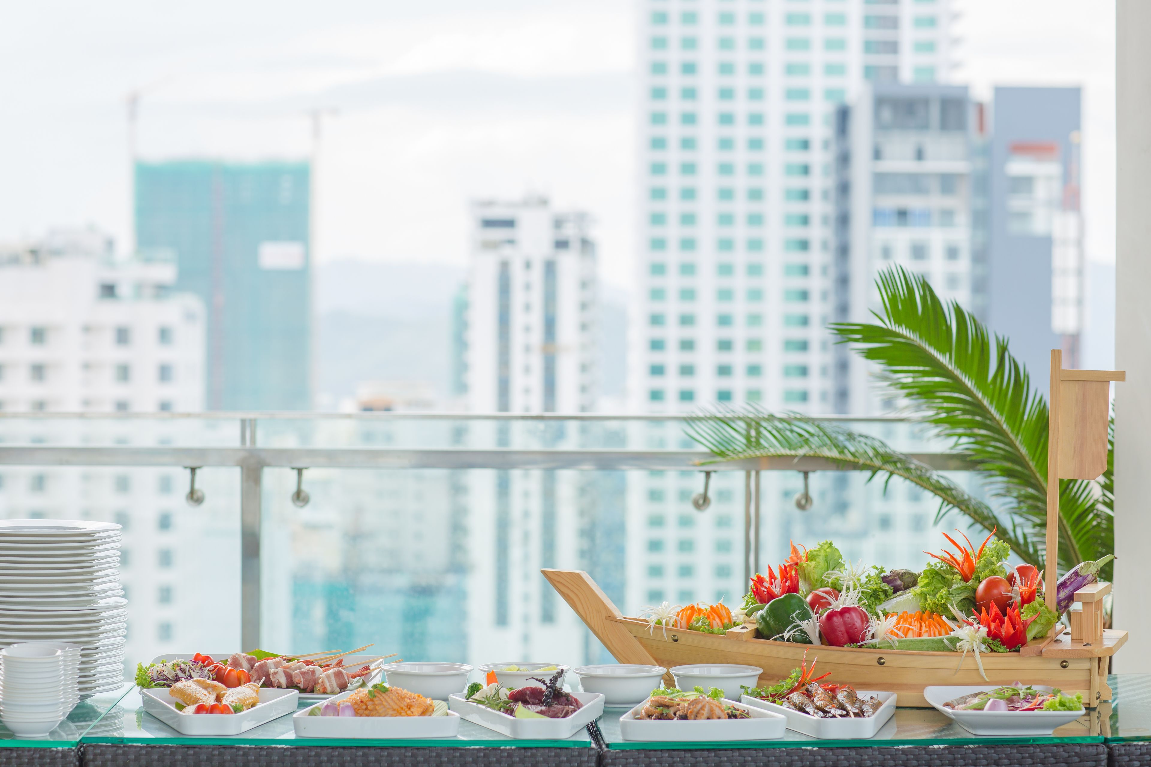 Una mesa de buffet con diversos platos y una decoración de barco de madera, con vista al horizonte de una ciudad.