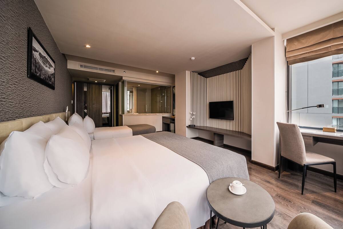 Habitación de hotel moderna con una cama grande, un televisor, una mesita y vistas a la ciudad.