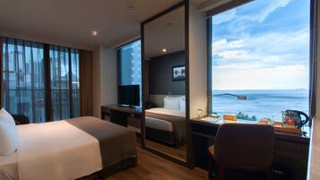A modern hotel room with a large bed, a desk, and a view of the sea.