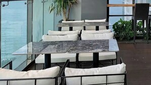 Een terras met buitenmeubilair, een palmpboom en uitzicht op zee.