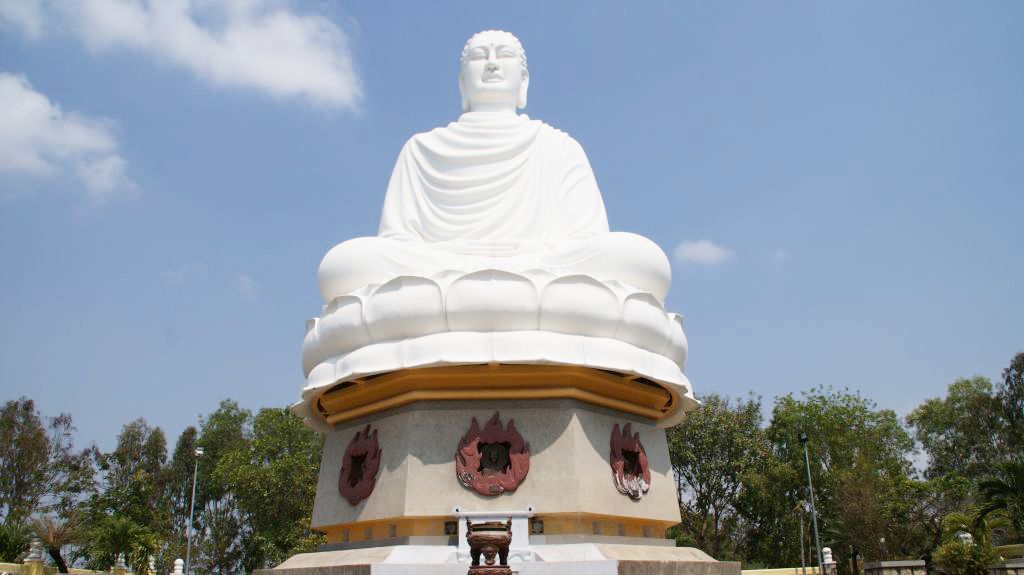 A large white Buddha statue with a golden base and three red circular decorations.
