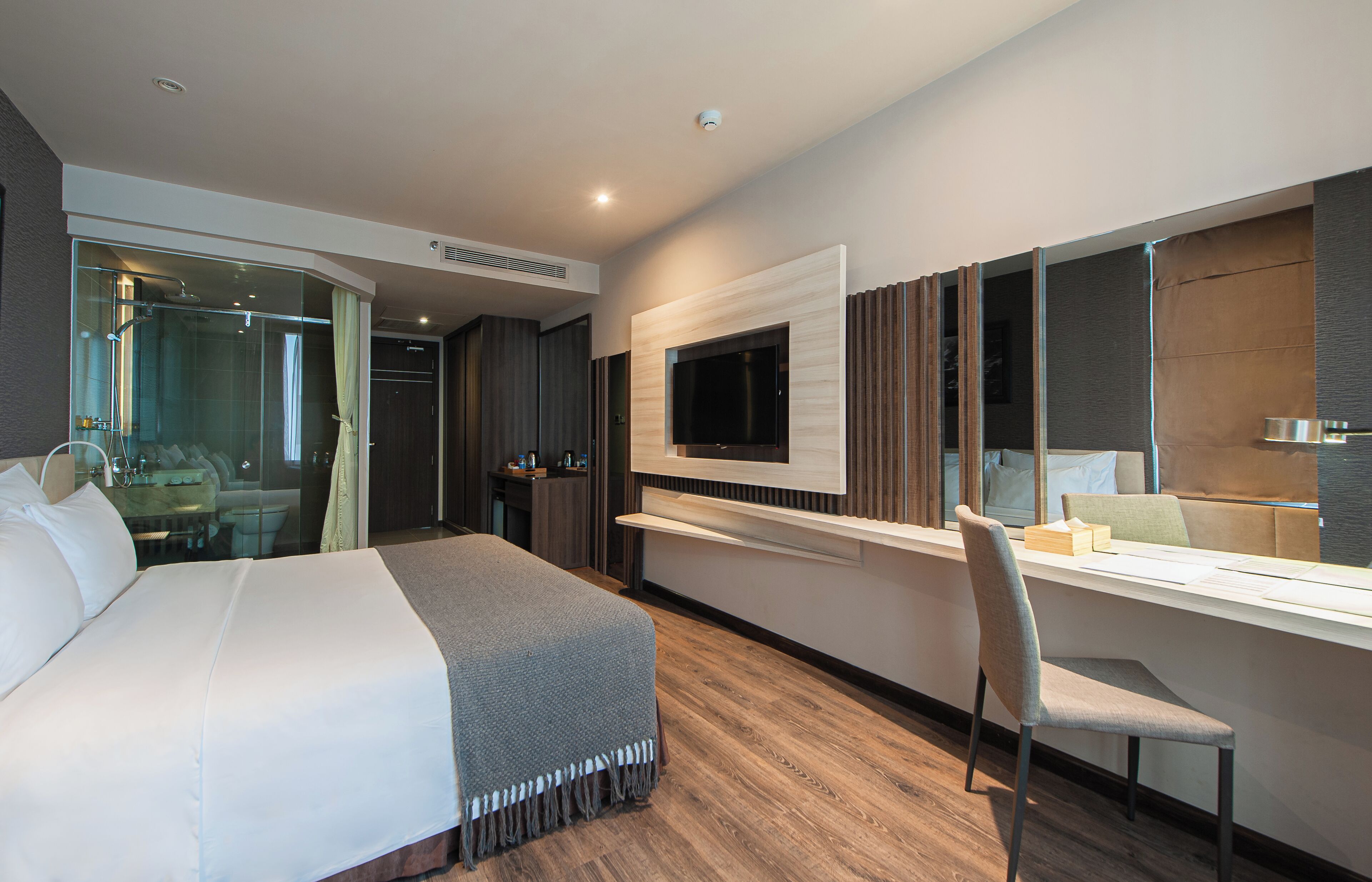 Una habitación de hotel moderna con una cama grande, un escritorio con silla, un televisor montado en la pared y cabina de ducha de vidrio.