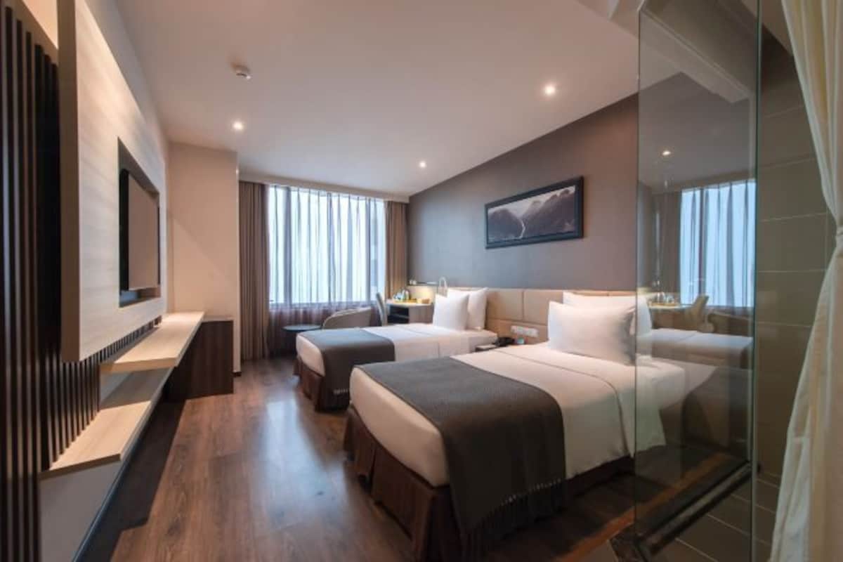 A hotel room with two beds, a flat-screen TV, a large window with curtains, and a painting on the wall.
