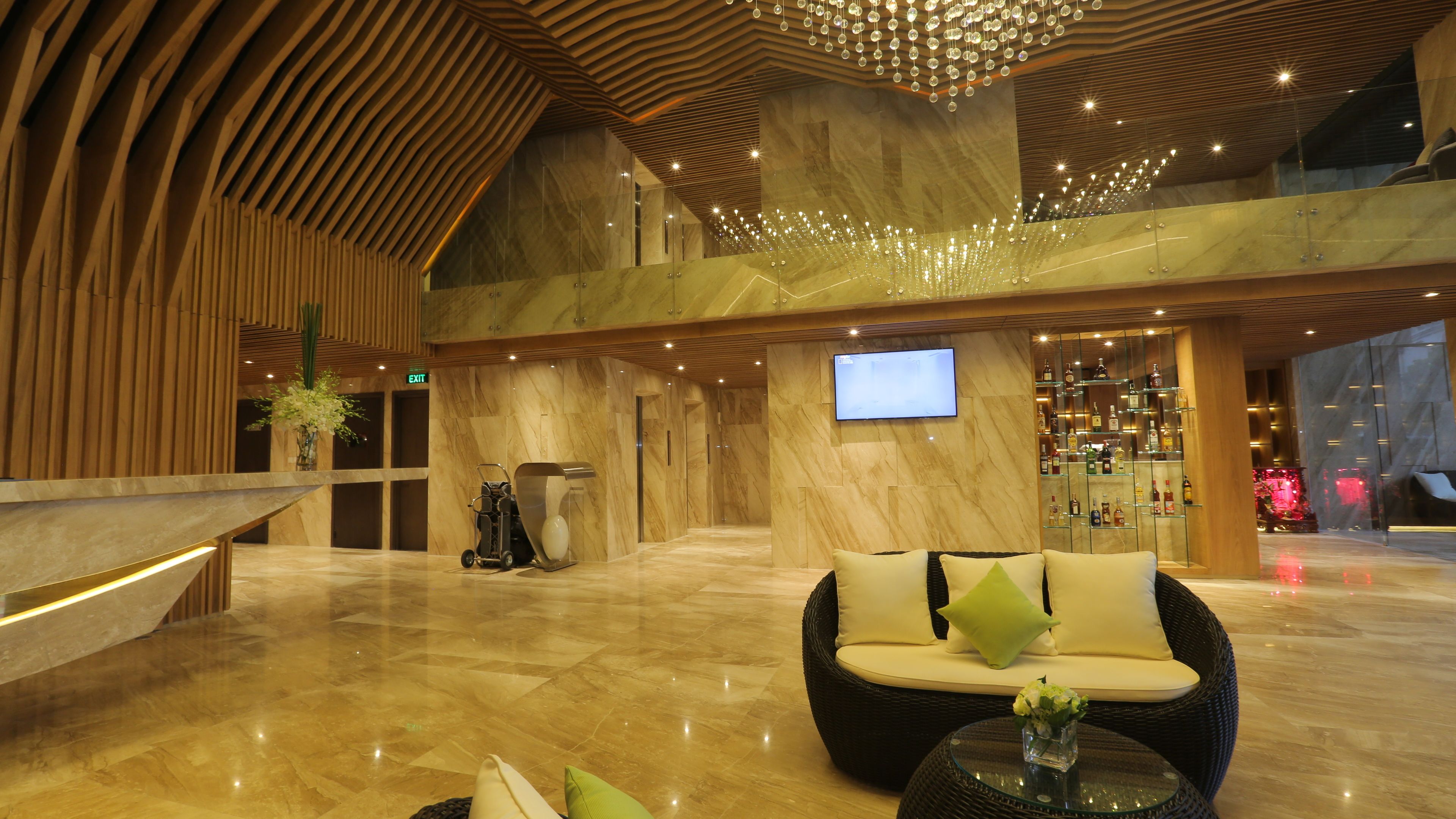 A spacious lobby with a high ceiling, marble flooring, a seating area with cushions, a television mounted on the wall, and a bar with shelves of bottles.