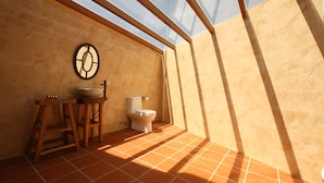 A bathroom with a skylight, a wooden stool, a sink, and a toilet.