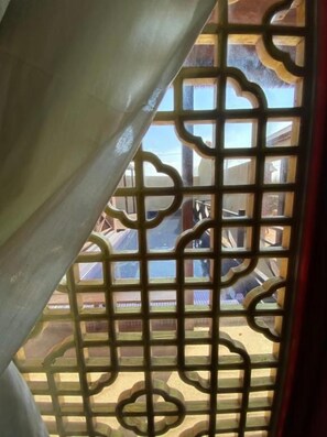 A view through a window with a decorative metal grille, a curtain partially covering the window, and a glimpse of the outside building structure. - Murraya Paniculata Villa (Magong)