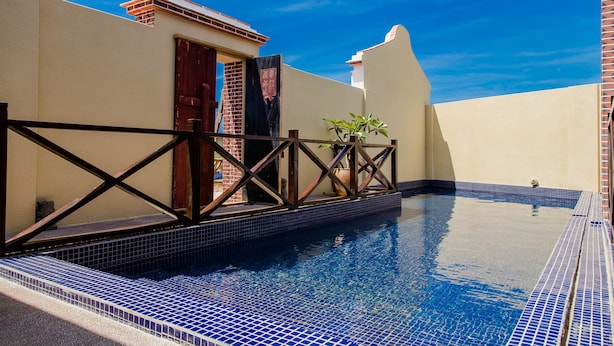 A swimming pool with blue tiles, a wooden deck, and a brick wall.