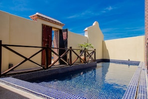 A swimming pool with blue tiles, a wooden deck, and a brick wall.