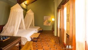 A room with two beds, a wooden table, a bench, and a tiled floor.