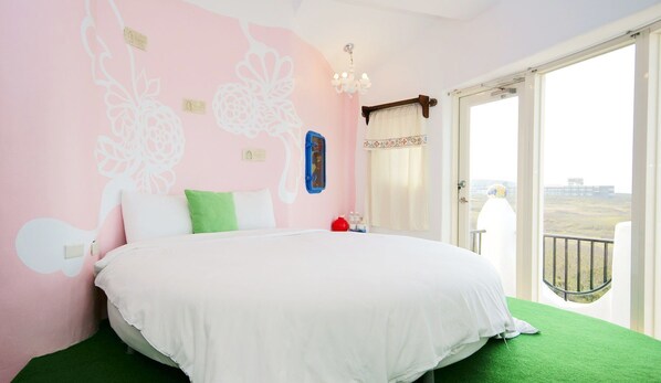 Quarto com uma cama grande, parede rosa com estampas florais, janela com vista e varanda com guarda-corpo.