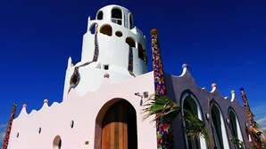 Un bâtiment à la façade blanche et rose, doté de nombreuses fenêtres en arc de cercle et d’une tour imposante.