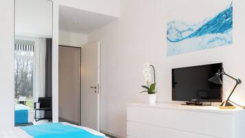 Una habitación de hotel moderna con una cama, un escritorio con televisión, una lámpara y un cuadro en la pared.