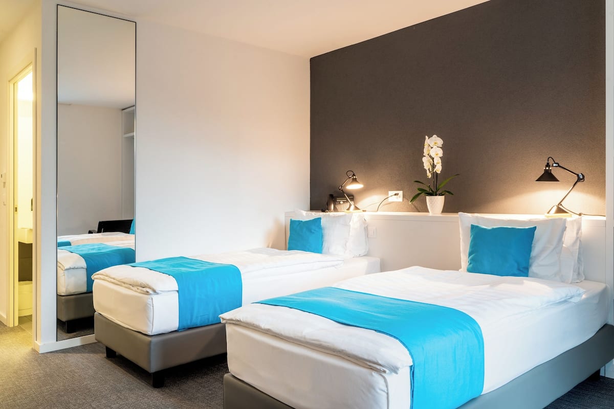 Habitación de hotel con dos camas, un espejo grande, una orquídea en maceta y lámparas de noche.